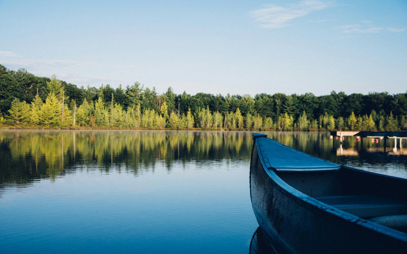 grey canoe on calm body of water near tall trees at daytime by Aaron Burden courtesy of Unsplash.