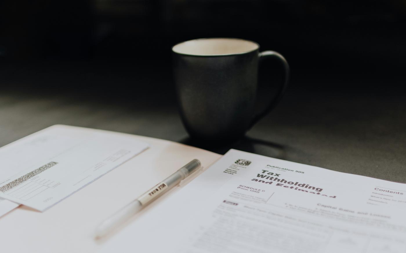 coffee mug near open folder with tax withholding paper by Kelly Sikkema courtesy of Unsplash.