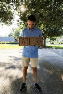 man in blue and white crew neck t-shirt holding brown wooden signage by Mick Haupt courtesy of Unsplash.