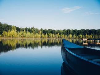 grey canoe on calm body of water near tall trees at daytime by Aaron Burden courtesy of Unsplash.